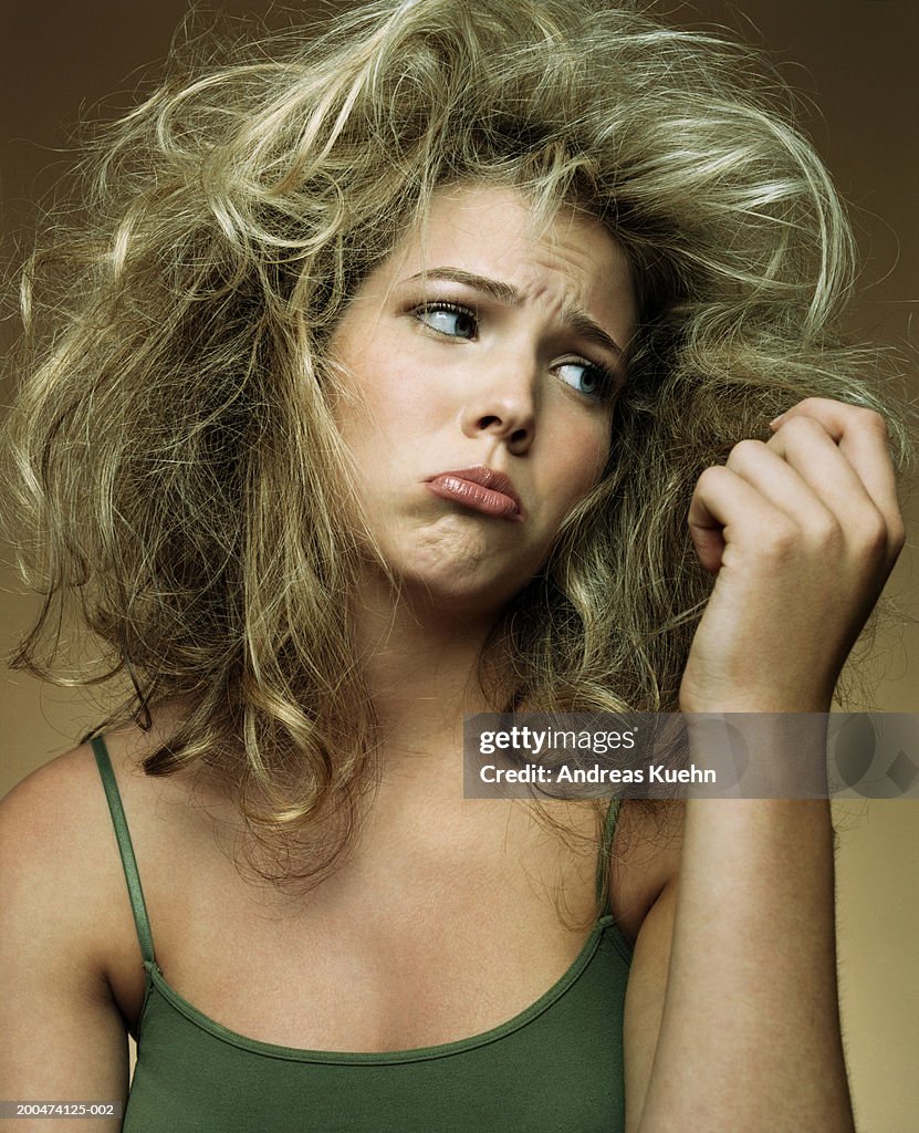 Teenage girl (15-17) looking at hair ends, making face