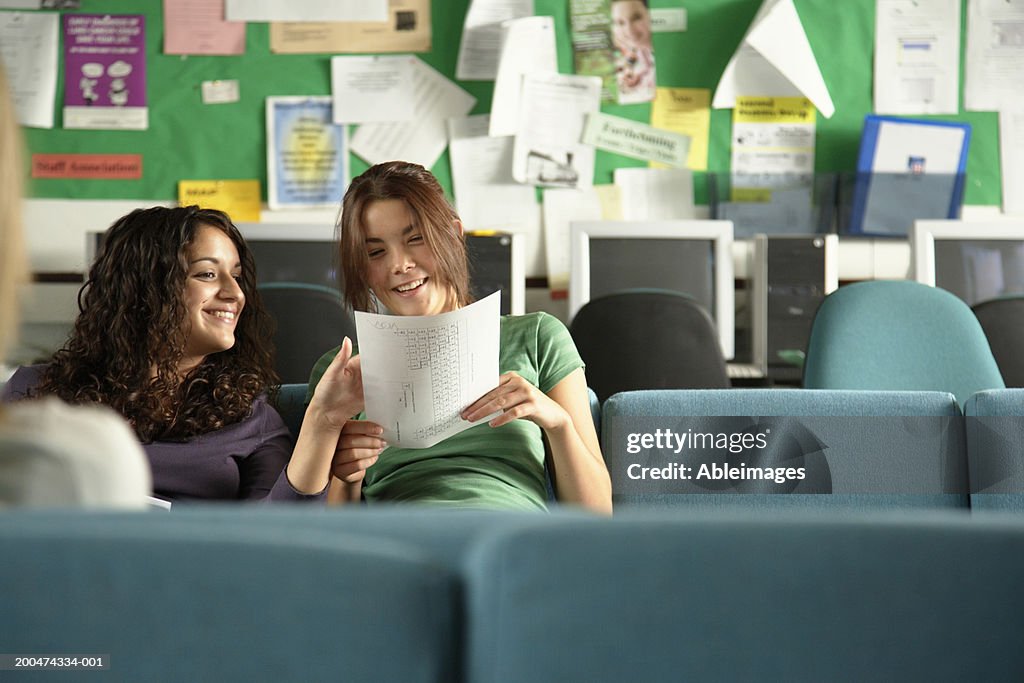 "Two teenage girls (16-18) in common room looking at paper, smiling"