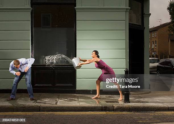 young woman throwing bucket of water over man, outdoors - throwing fotografías e imágenes de stock