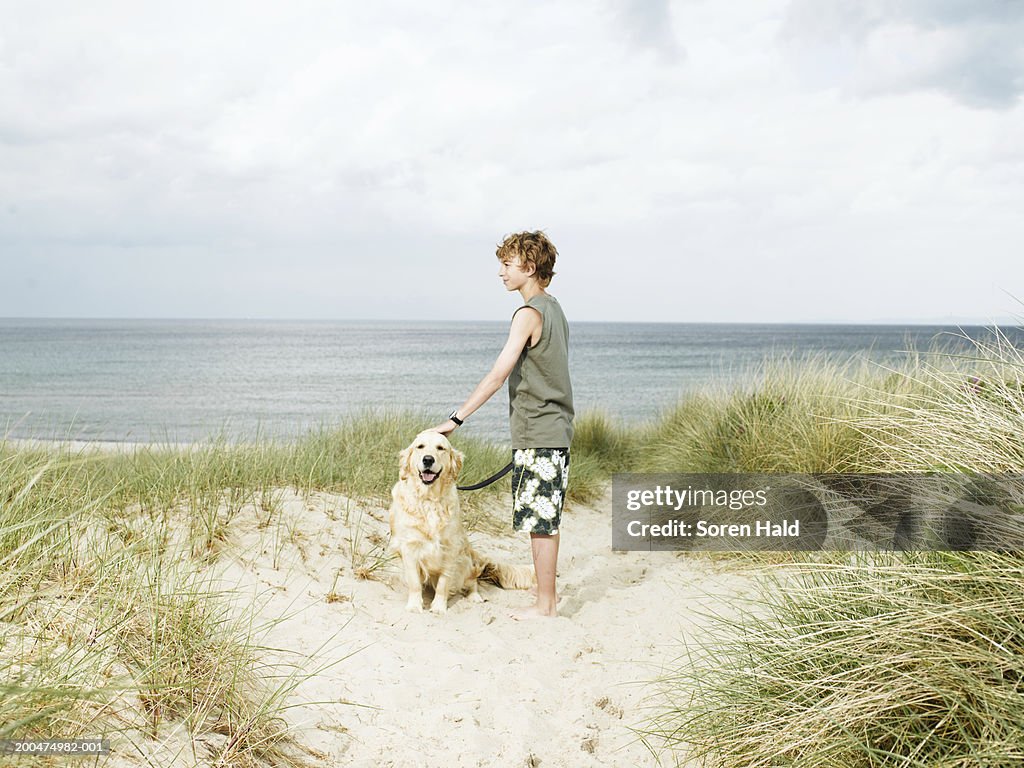 Boy (10-12) standing in sand dunes holding dog on lead