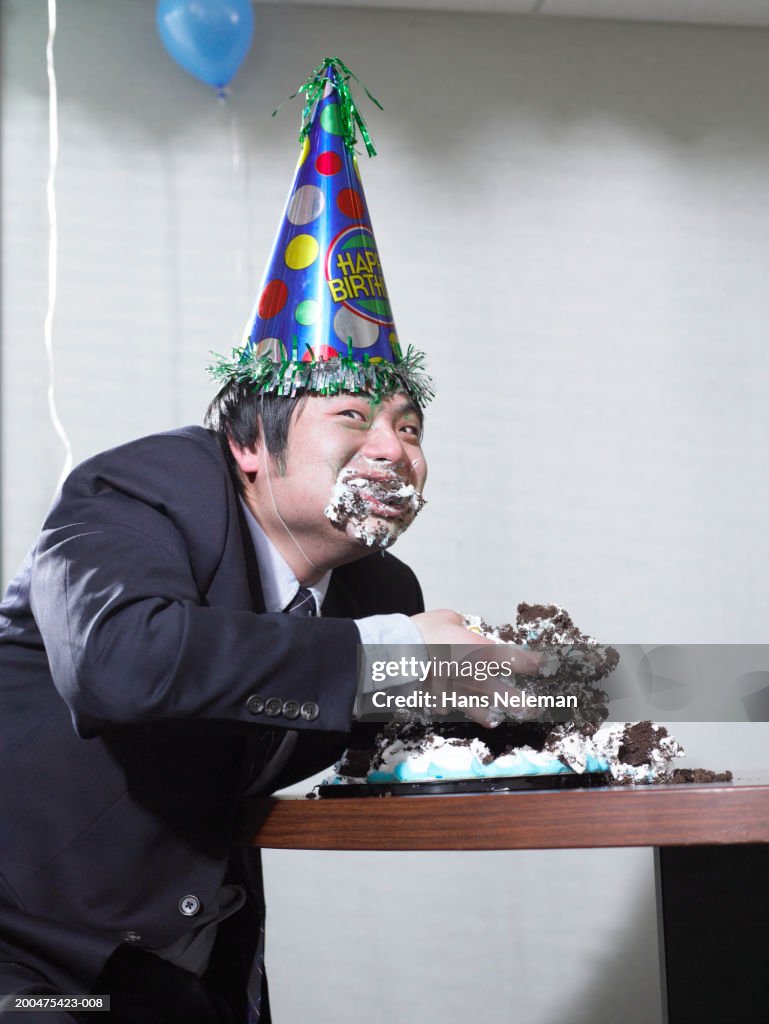 Businessman eating birthday cake with hands, stuffing face