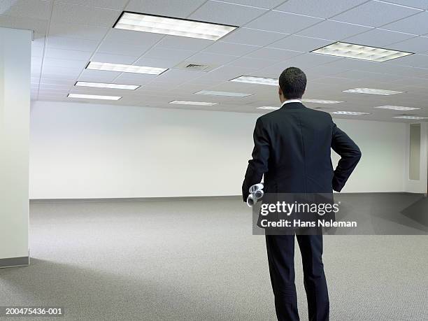 businessman with rolls of plans, standing in empty office, rear view - encuadre de tres cuartos fotografías e imágenes de stock