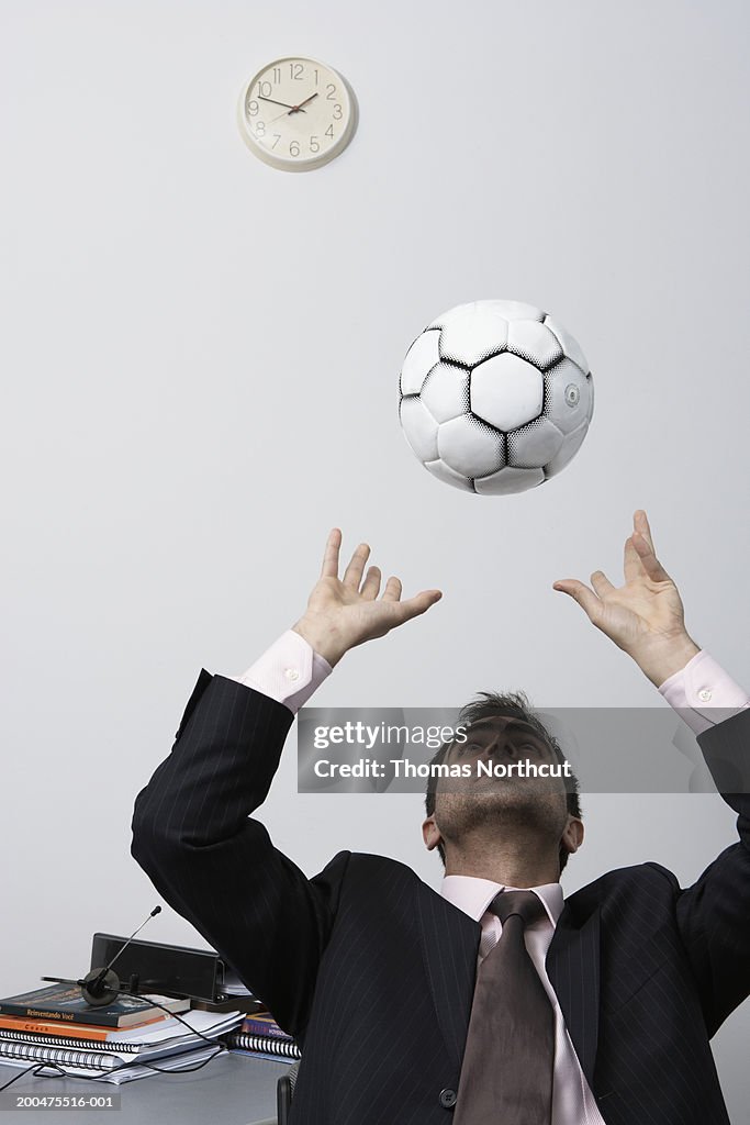 Businessman playing with soccer ball at desk, looking up