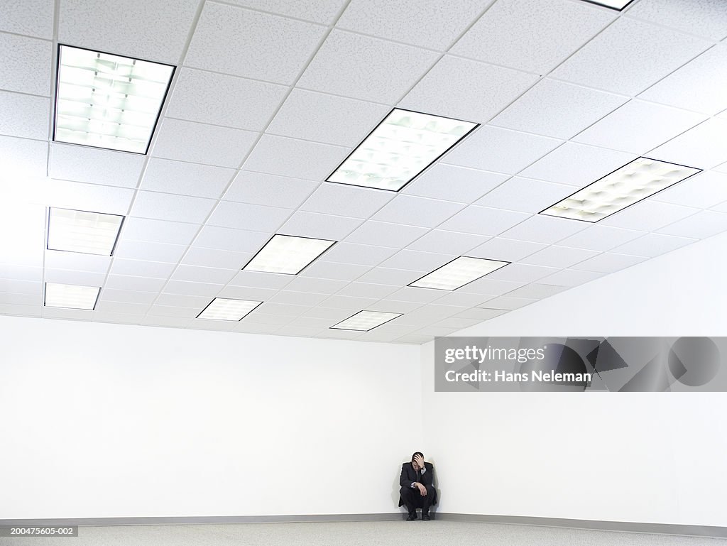 Businessman crouching in corner of empty office space