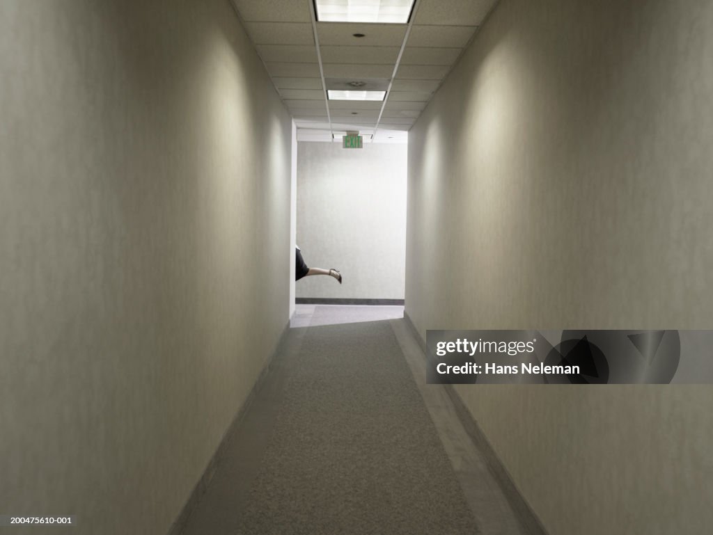 Businesswoman running at end of corridor, low section, side view