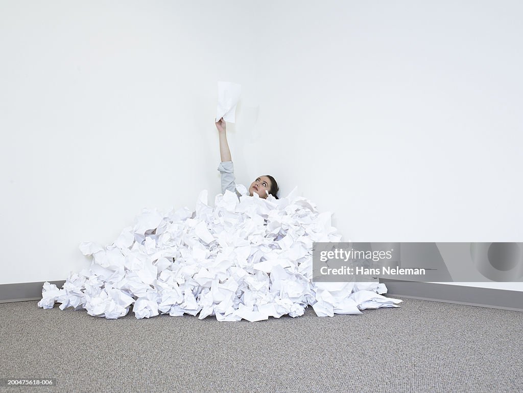 Businesswoman covered in pile of papers holding paper upwards
