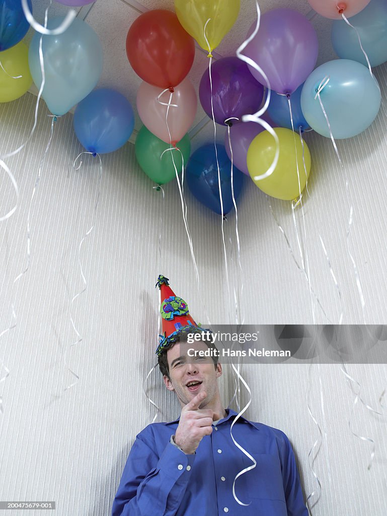 Businessman wearing party hat, holding balloons