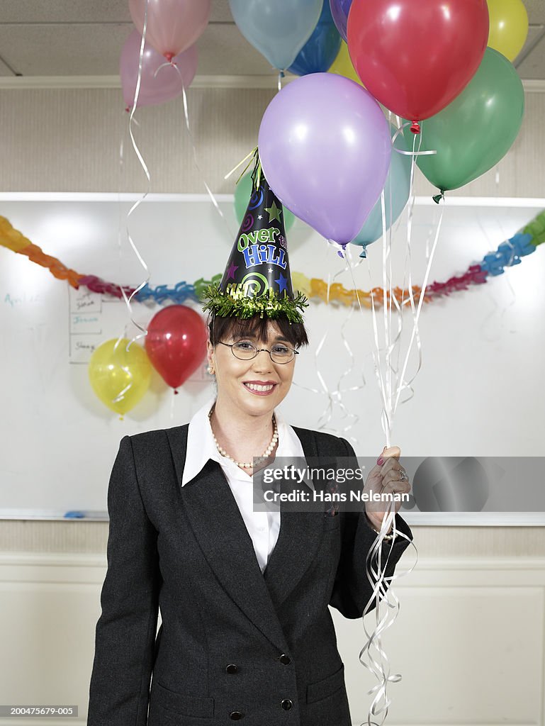 Businesswoman wearing party hat, holding balloons, portrait