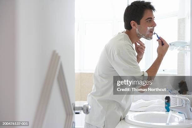 man shaving face in bathroom mirror, side view - scheren stockfoto's en -beelden