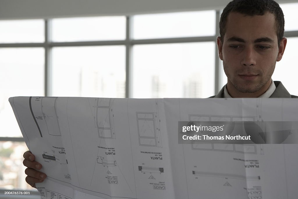 Young businessman looking at blueprint in office building