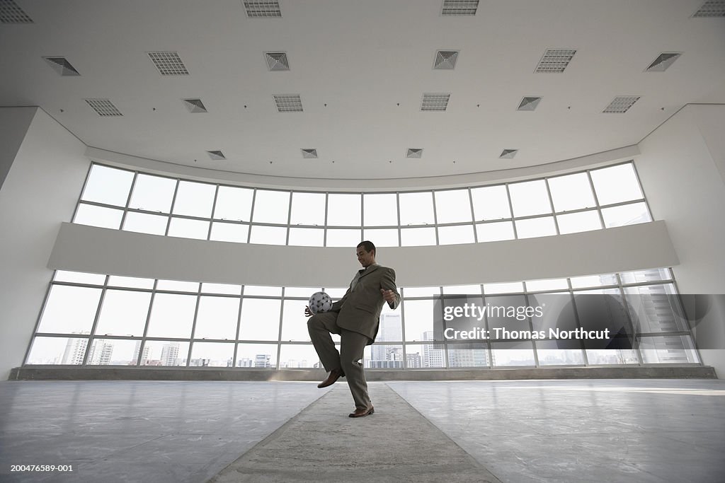 Young businessman playing with soccer ball in empty office, side view