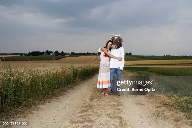 young couple standing by field, man wearing bull mask - hoorn stockfoto's en -beelden