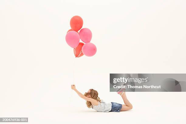 girl (8-10) lying on stomach, holding bunch of balloons, side view - balloon stomach stockfoto's en -beelden