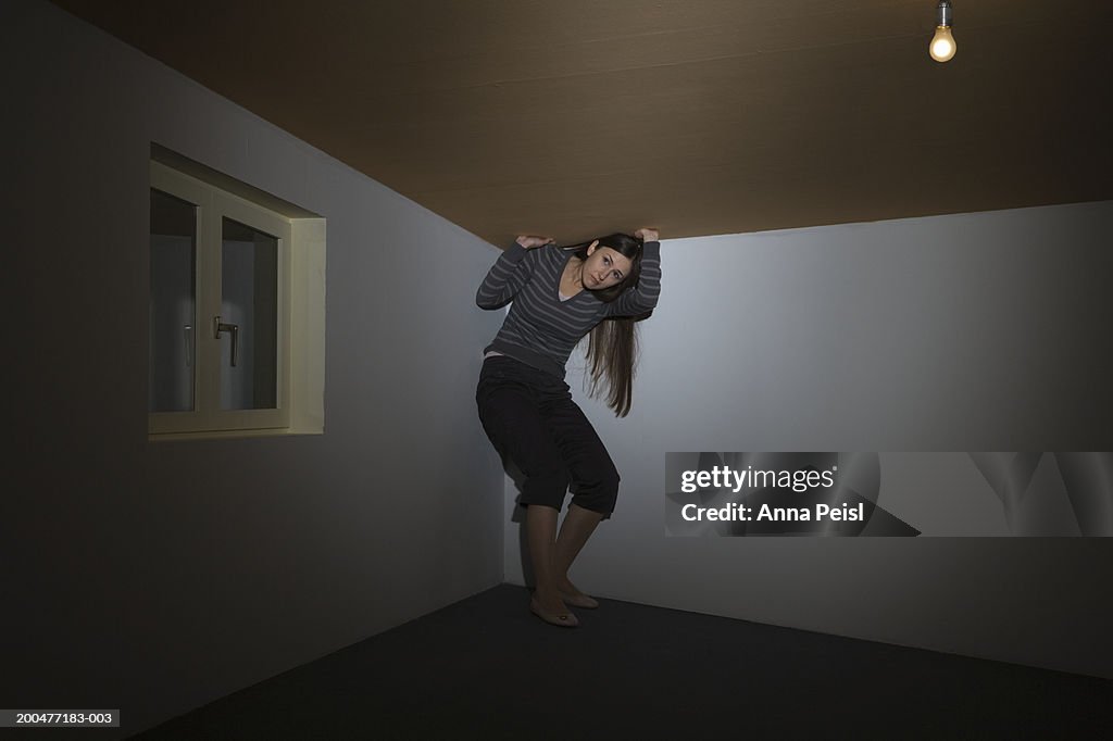 Woman trying to stand under low ceiling in room lit by single bulb