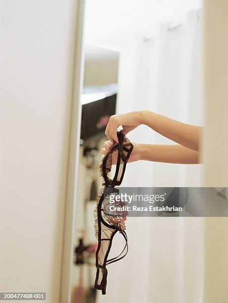 young woman holding bra in dressing room - bra fotografías e imágenes de stock