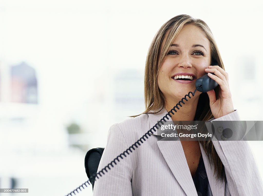 Young businesswoman using telephone in office, smiling
