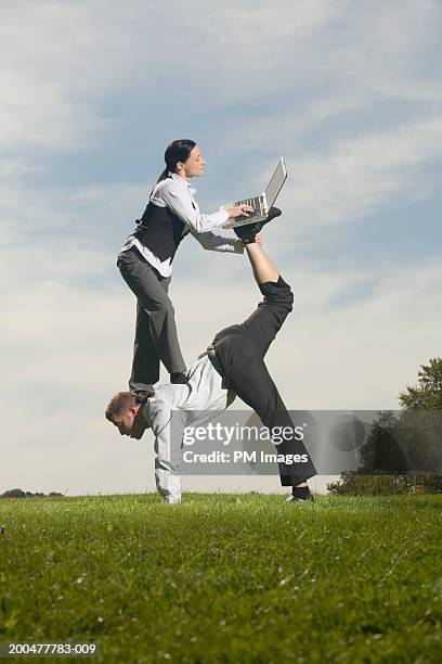 businesswoman balancing on man's back, using laptop, side view - businesswoman handstand stock-fotos und bilder