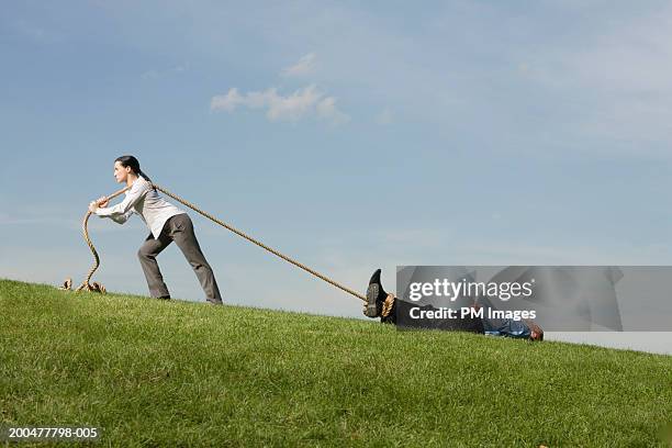 businesswoman dragging businessman across field with rope, side view - traîner photos et images de collection