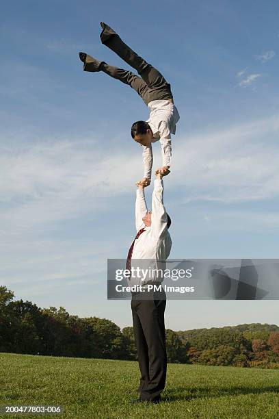 businessman supporting woman doing handstand - businesswoman handstand stock pictures, royalty-free photos & images