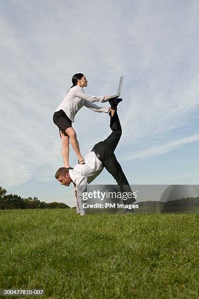 businesswoman on man's back using laptop balanced on man's feet - businesswoman handstand stock-fotos und bilder