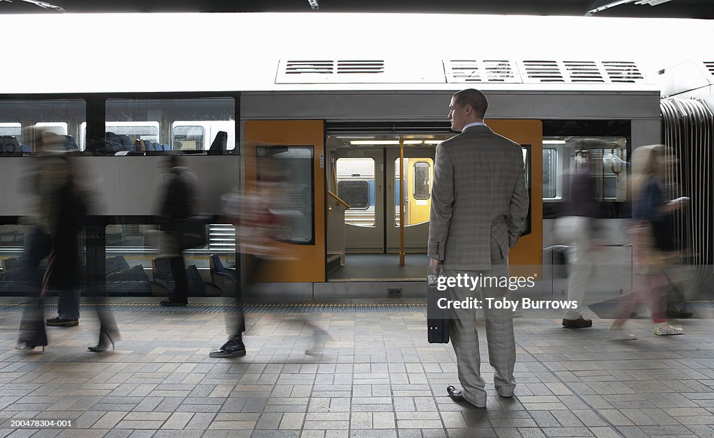 Commuters passing businessman on platform, (blurred motion)