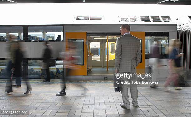 commuters passing businessman on platform,  (blurred motion) - railroad station stock pictures, royalty-free photos & images