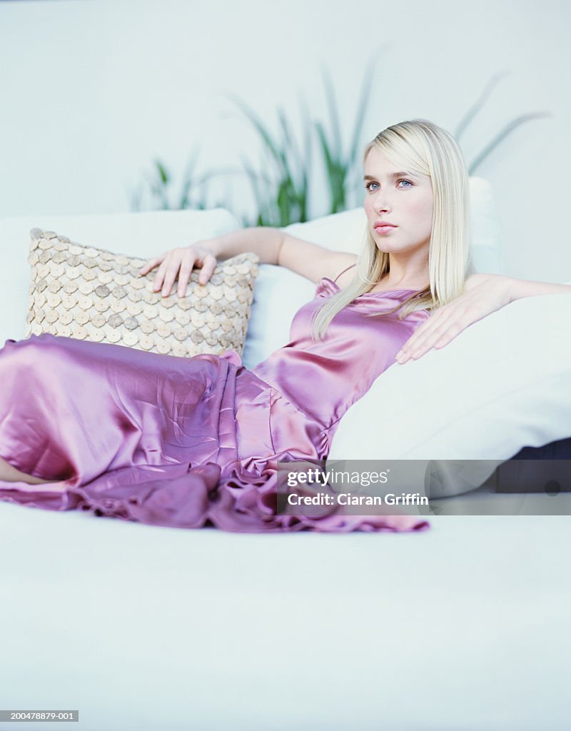 Young woman wearing evening dress relaxing on sofa, portrait