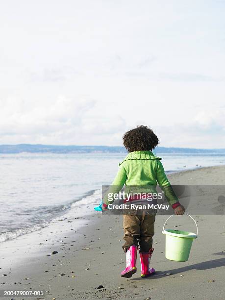 girl (5-7) carrying bucket and shovel on beach, rear view - beach shovel stockfoto's en -beelden