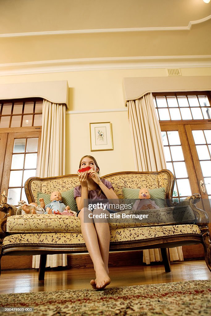 Girl (8-10) sitting on sofa, eating cake, low angle view