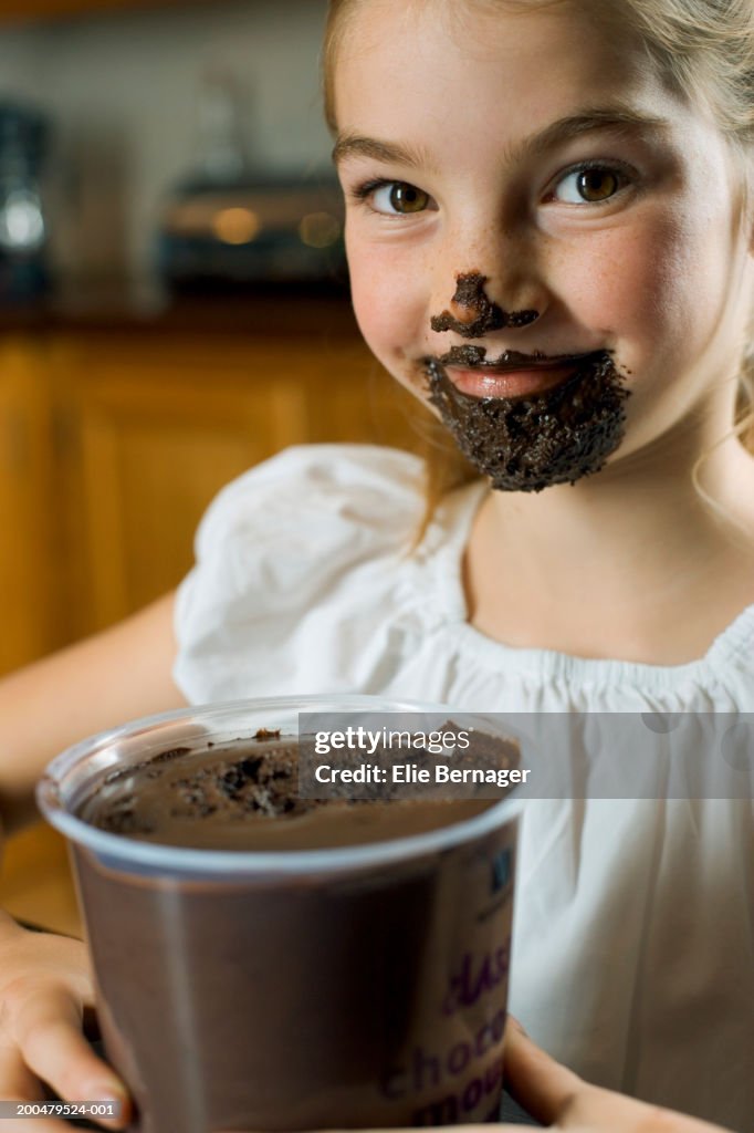 Girl (8-10) eating chocolate mousse, smiling, portrait