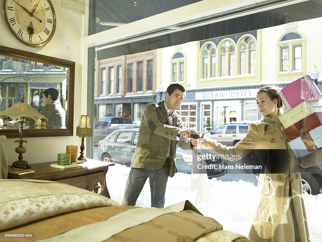 Woman carrying boxes, man handing her package outside furniture store