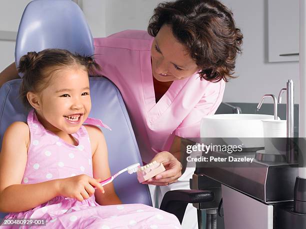 dental assiatant teaching girl (4-7) how to brush teeth, smiling - dentista bambini foto e immagini stock
