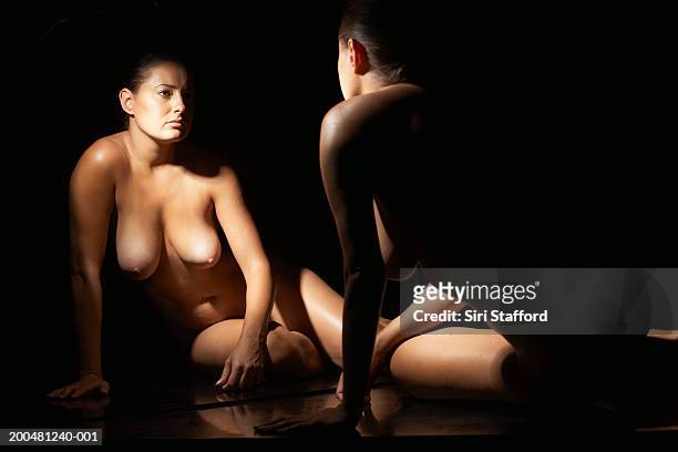 nude woman looking at reflection in mirror - looking over shoulder stockfoto's en -beelden