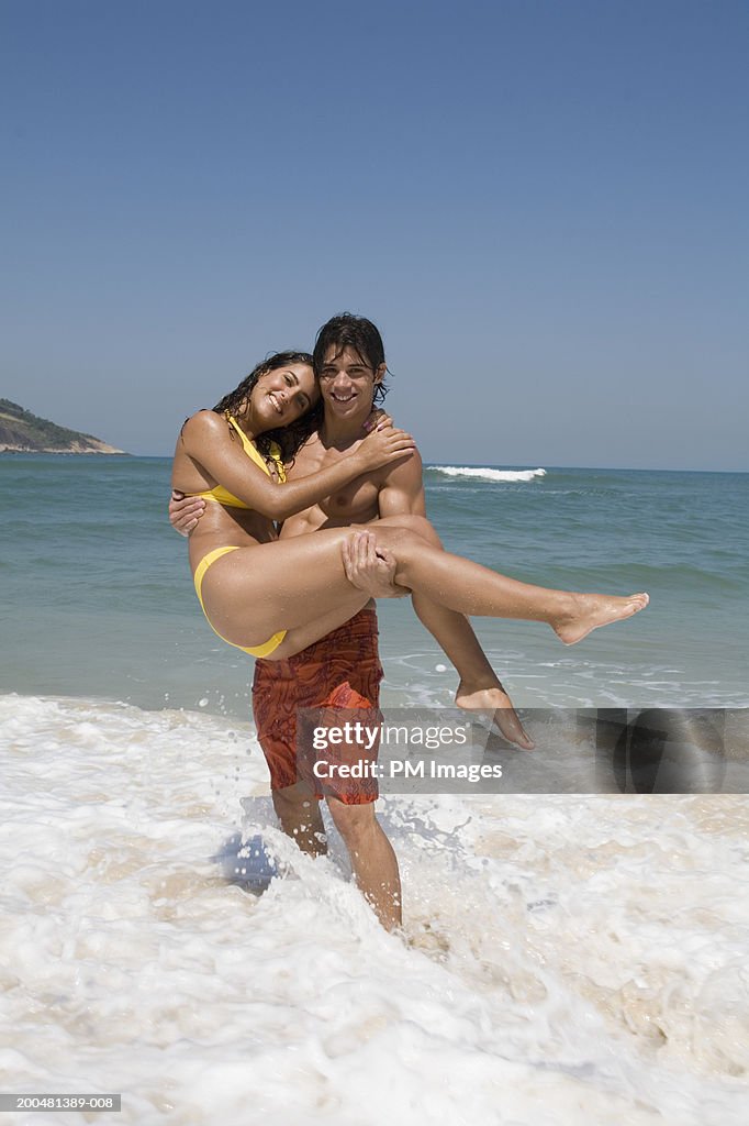 Young man carrying woman in surf, portrait