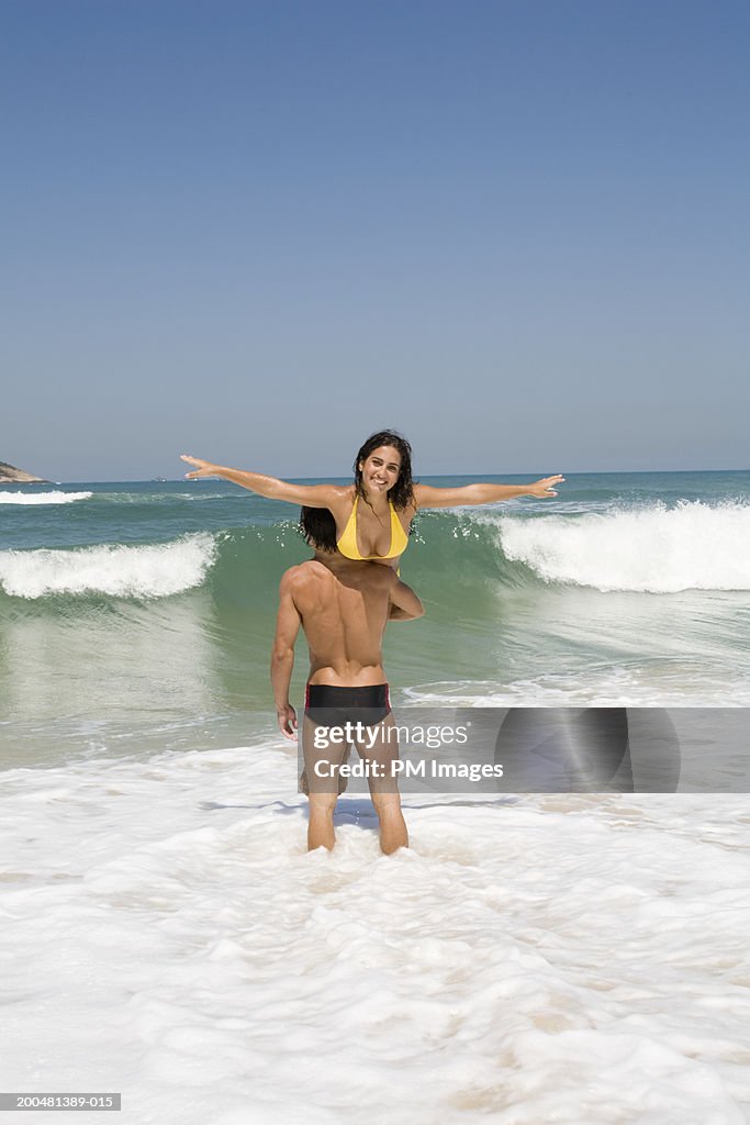 Young man lifting woman over shoulder in surf, rear view of man