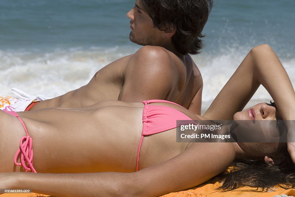 Young couple sunbathing at beach, side view