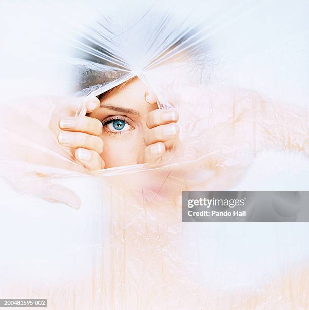 young woman tearing hole in plastic, close-up, portrait - tear face photos et images de collection