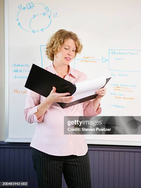 pregnant business woman standing by whiteboard, reading folder - teacher with folder stock pictures, royalty-free photos & images