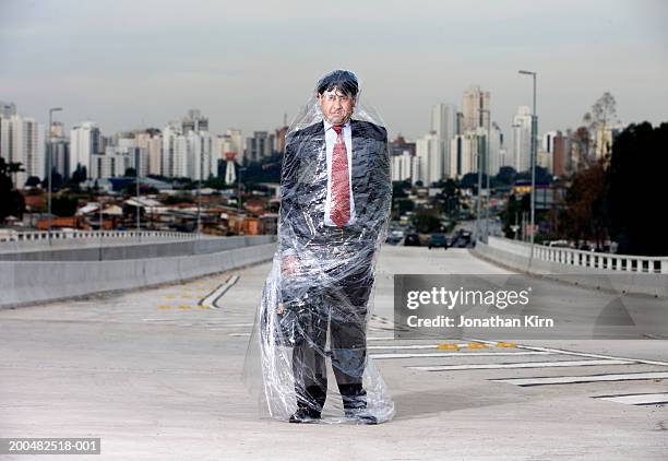 businessman wrapped in polythene standing on road - man wrapped in plastic stock pictures, royalty-free photos & images