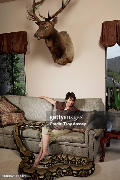 mature woman with python sitting on couch in living room - brown snake stockfoto's en -beelden