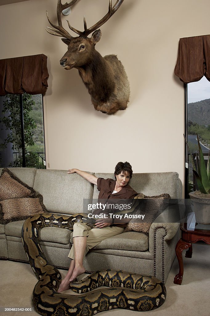 Mature woman with python sitting on couch in living room