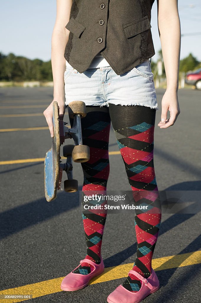 Teenage girl (16-18) holding skateboard, low section