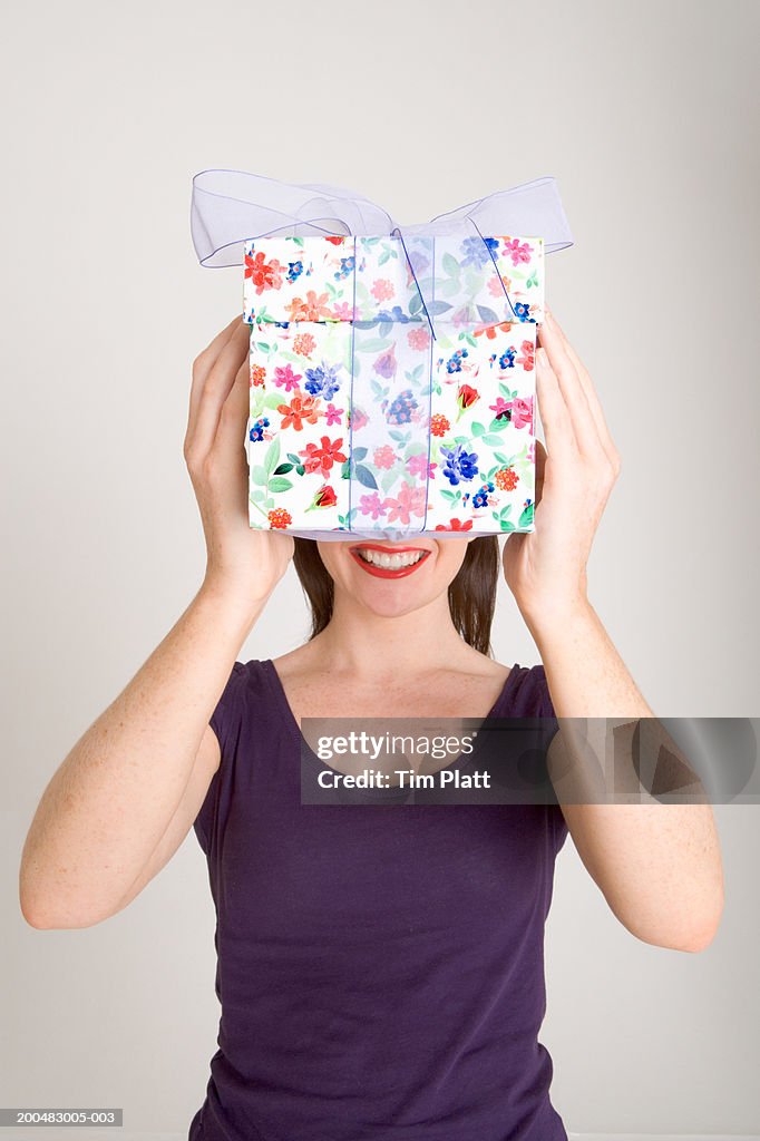 Woman holding gift box in front of face