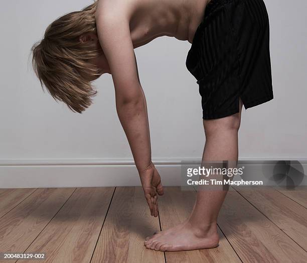 boy (6-8) standing indoors, reaching for toes, side view - 前屈運動 ストックフォトと画像