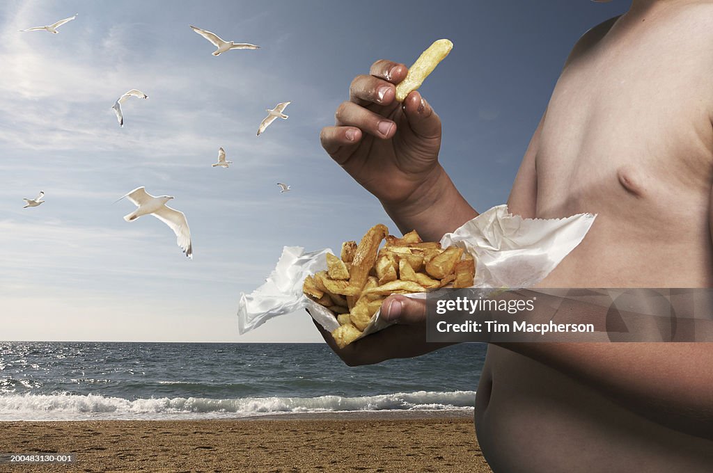 Boy (6-8) eating portion of chips at beach, mid section (Digital Composite)