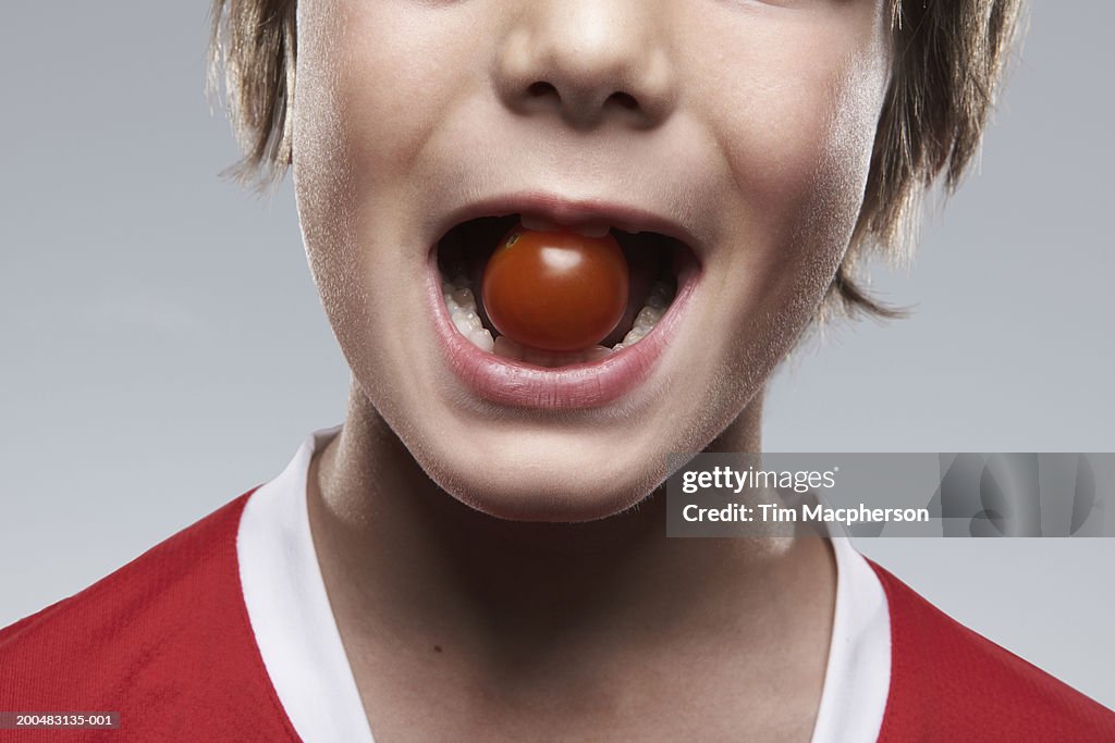 Boy (8-10) with tomato between teeth, close-up