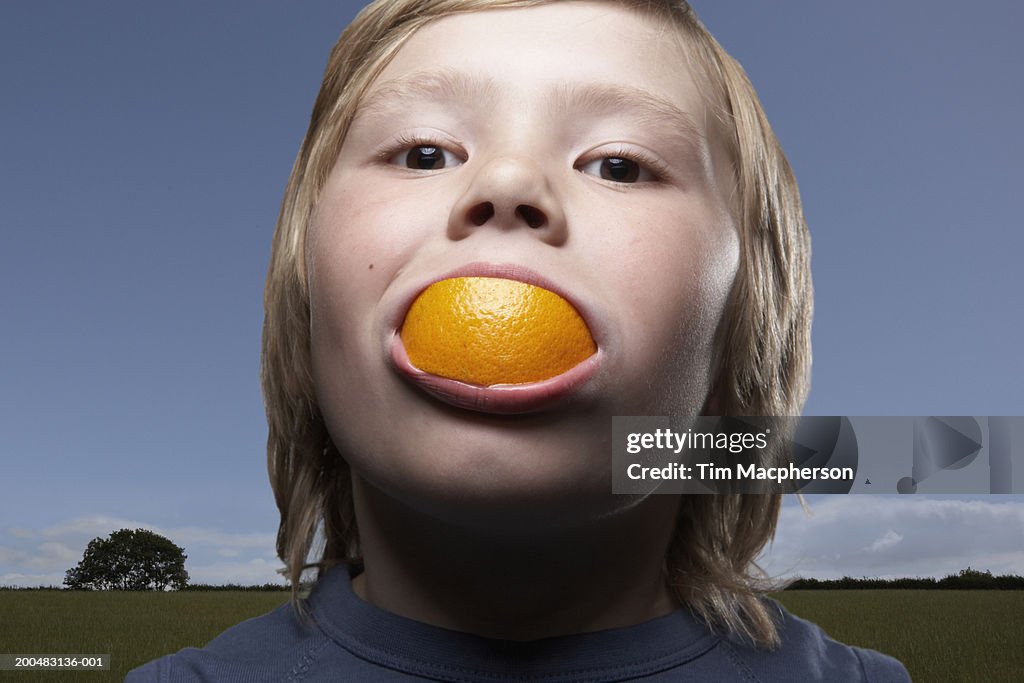 Boy (6-8) with orange wedge between teeth, outdoors, close-up, portrait (Digital Composite)