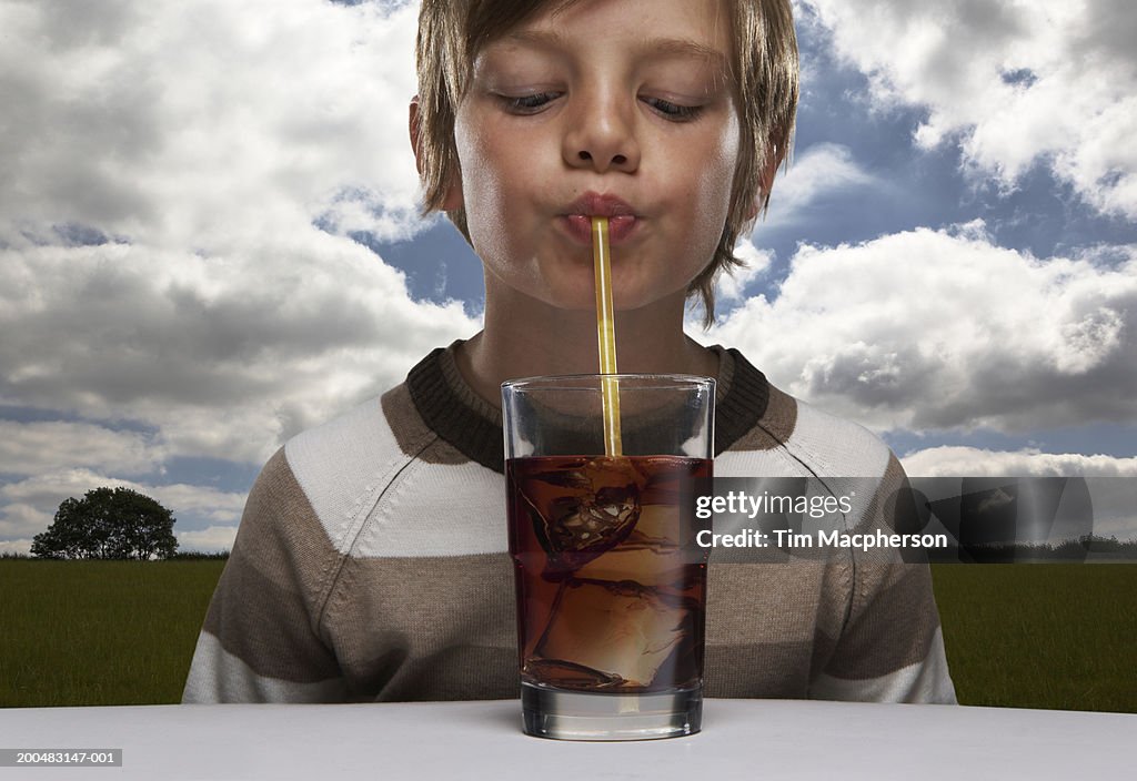 Boy (8-10) drinking glass of cola in countryside, close-up (Digital Composite)