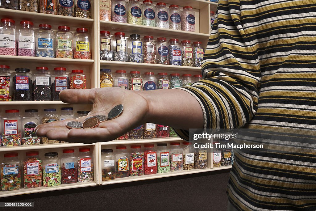 Boy (6-8) in sweetshop, holding out palm with loose change, close-up (Digital Composite)