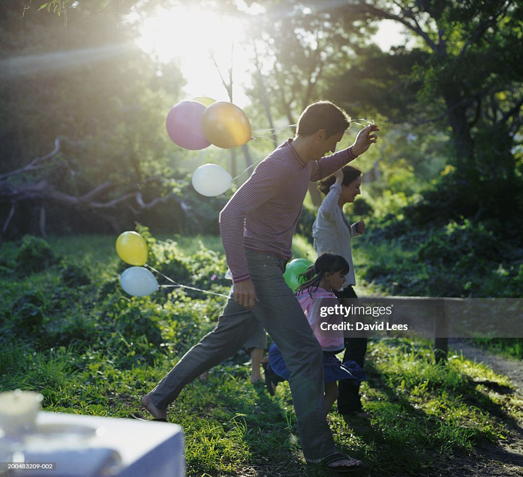 Parents with two children (6-7, 8-9) holding balloons, running through garden